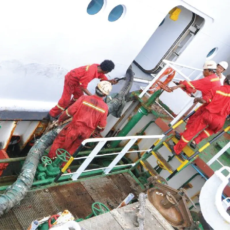 Crew in red overalls handling a fuel hose on a vessel deck